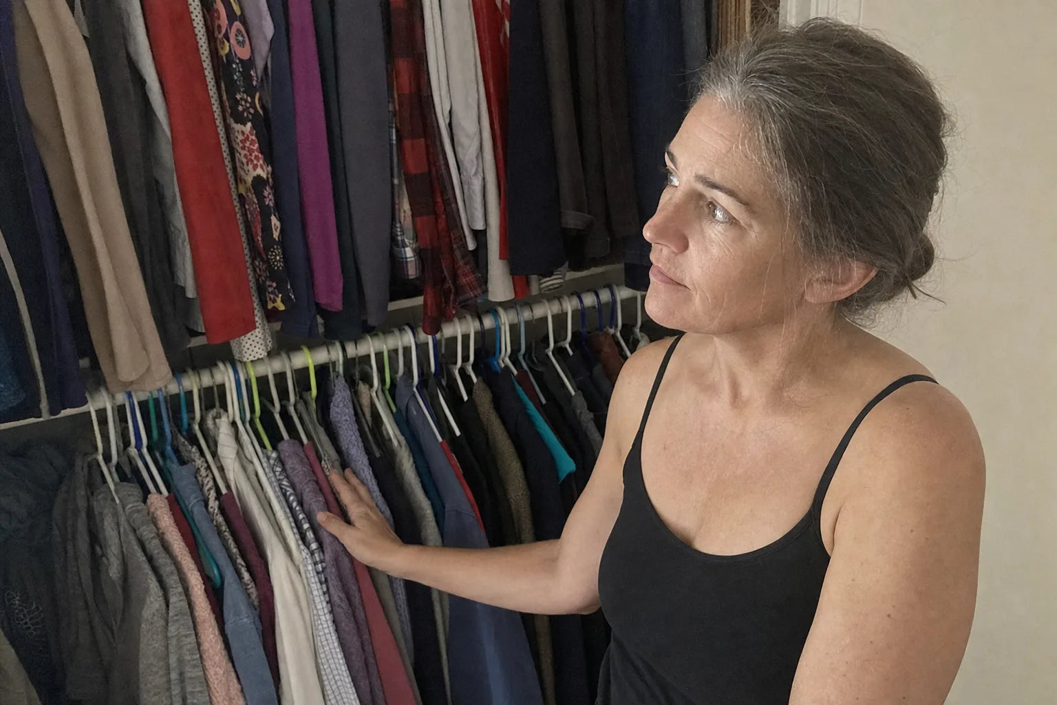 A woman's closet split into a smaller older wardrobe and a newer larger one, her hand resting on the smaller row