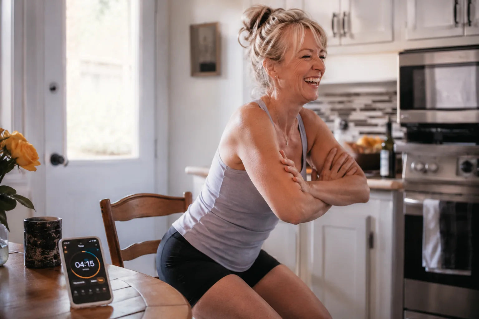 A woman laughing mid chair-stand in her kitchen